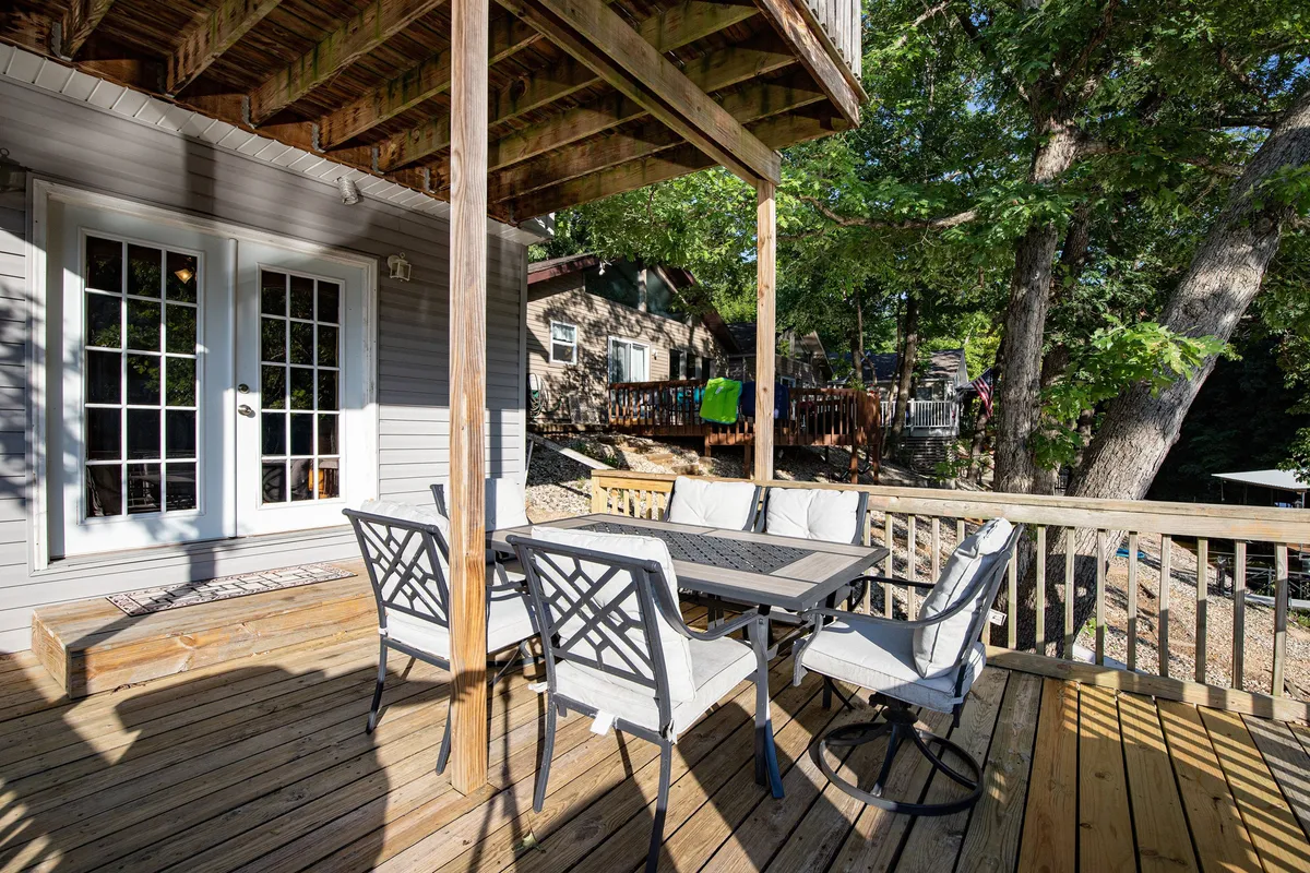 A cozy outdoor dining set sits atop a spacious deck surrounded by trees, inviting families to gather for meals while looking out over the water. The deck rail hints at elevation, offering a lovely vantage point of the natural surroundings.