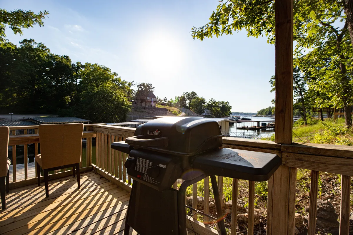 A spacious deck overlooks the water, furnished with comfortable chairs and a grill. The scene invites gatherings with friends for barbecuing, relaxing, and soaking in the views of the lake, suggesting a lively yet laid-back atmosphere perfect for socializing.