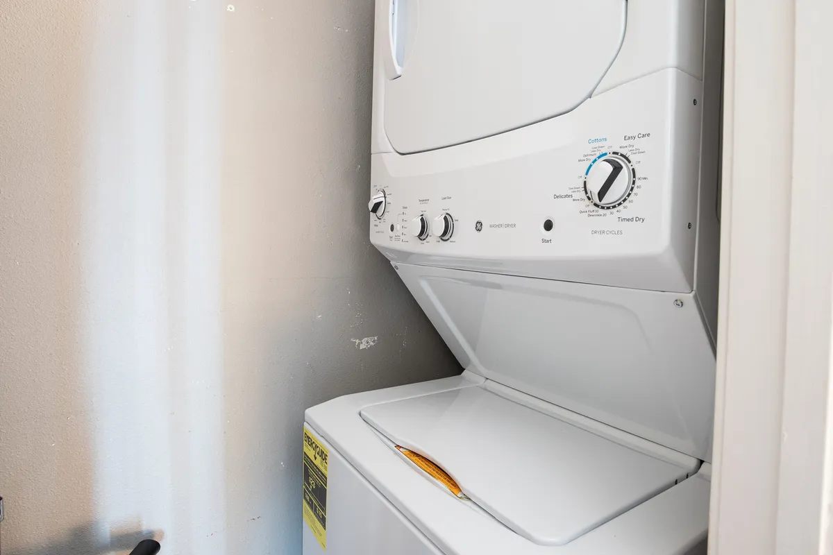 A modern stacked washer and dryer set in a bright, utilitarian nook. The appliances are neatly integrated and easily accessible, providing practical in-unit amenities for guests' convenience.