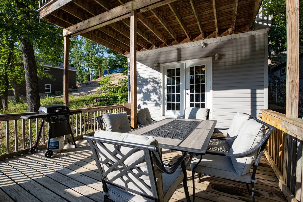 An outdoor dining table with comfortable seating and a grill is displayed on a deck, surrounded by nature. The setup is ideal for al fresco dining, socializing, and enjoying sunset views.