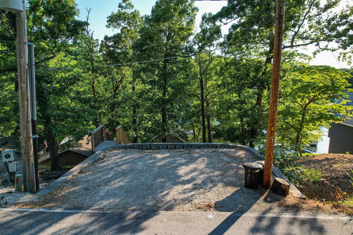 A gravel driveway flanked by tall trees, hinting at open space for parking and access to natural trails. The atmosphere is tranquil, with glimpses of the surrounding forest and sky, inviting guests and their pets to begin their adventure right from the doorstep.