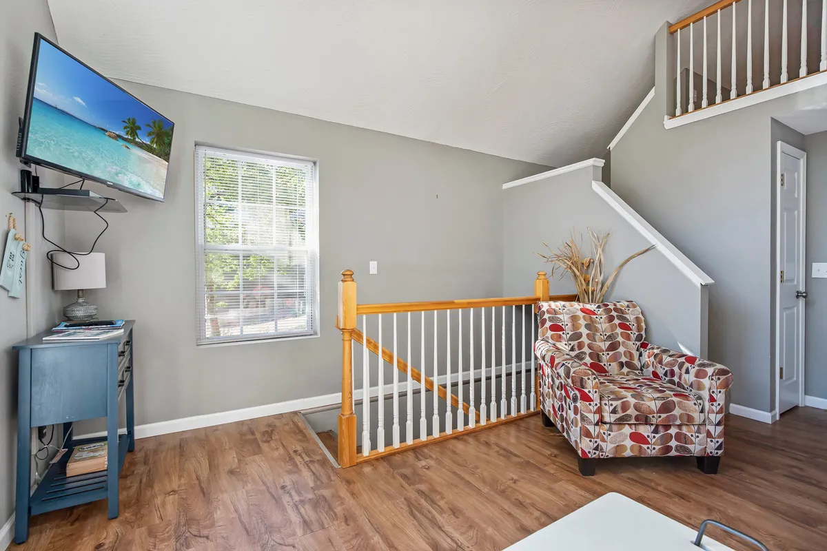 A cozy corner featuring a colorful armchair, television, and a window letting in abundant daylight. The room is styled to feel intimate and inviting, ideal for unwinding after a day at the lake or settling in for a movie night.