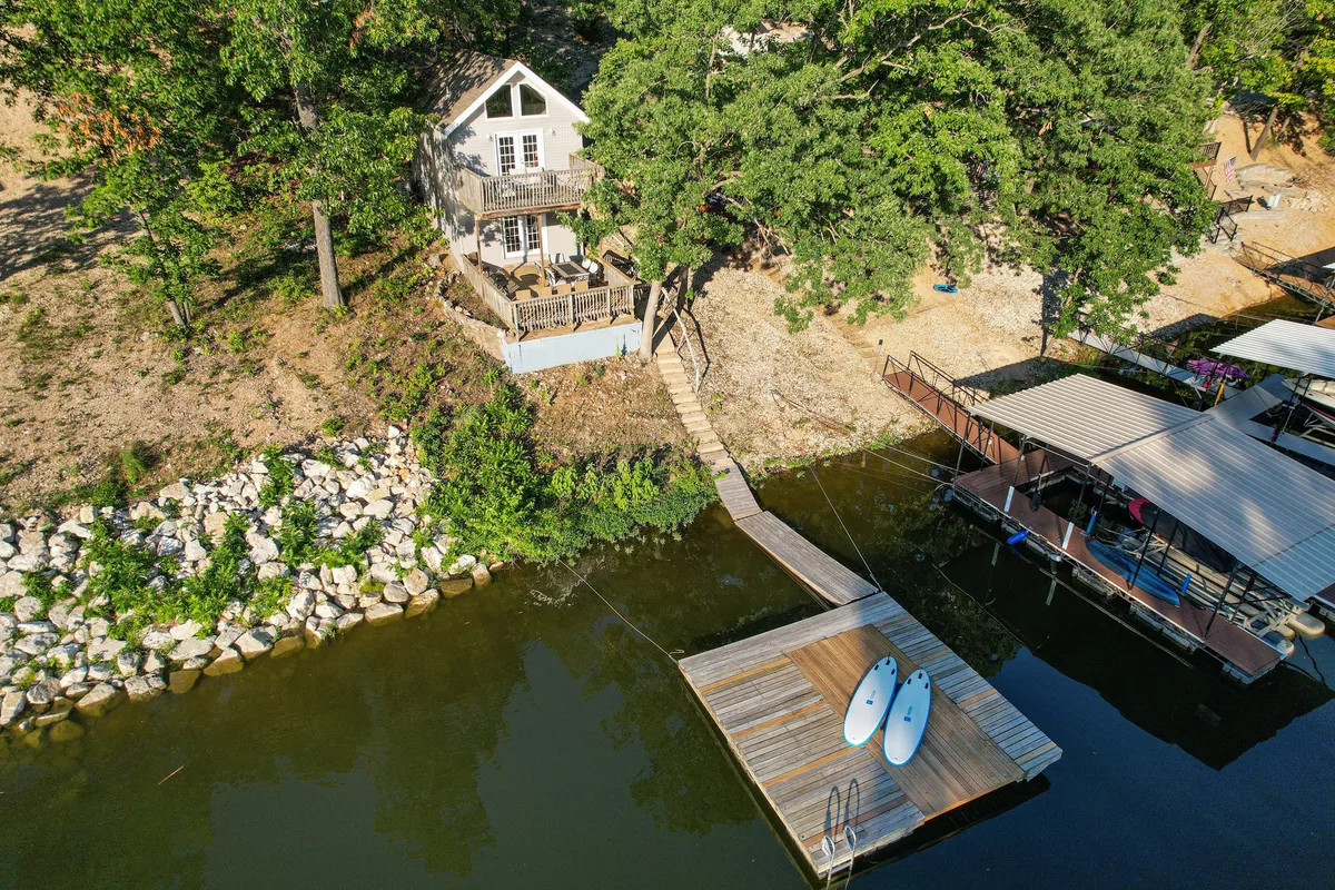 A wide-angle view showcases the house situated right by the lake, the private dock, and several paddleboards at the water’s edge. The scene hints at easy transitions from indoor comfort to outdoor excitement, with calm water ready for new adventures.